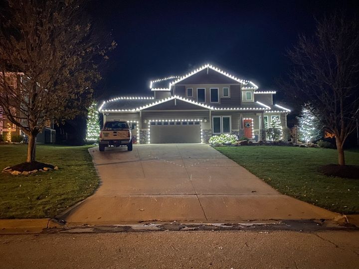 A two-story craftsman home with every roof line, the garage door and front door outlined in bright white bulbs, a Strahm Lawns truck in the driveway