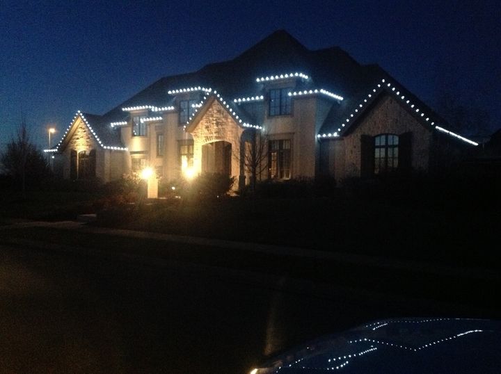 A large stone and stucco estate with cool white bulbs outlining each dormer, gable and roof edge at dusk