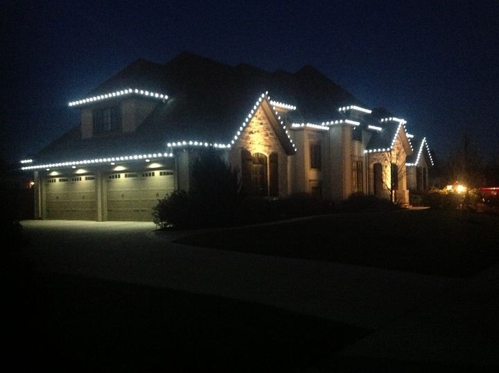 A large home at dusk with cool white C9 bulbs along every roof edge, gable and dormer above a three-car garage